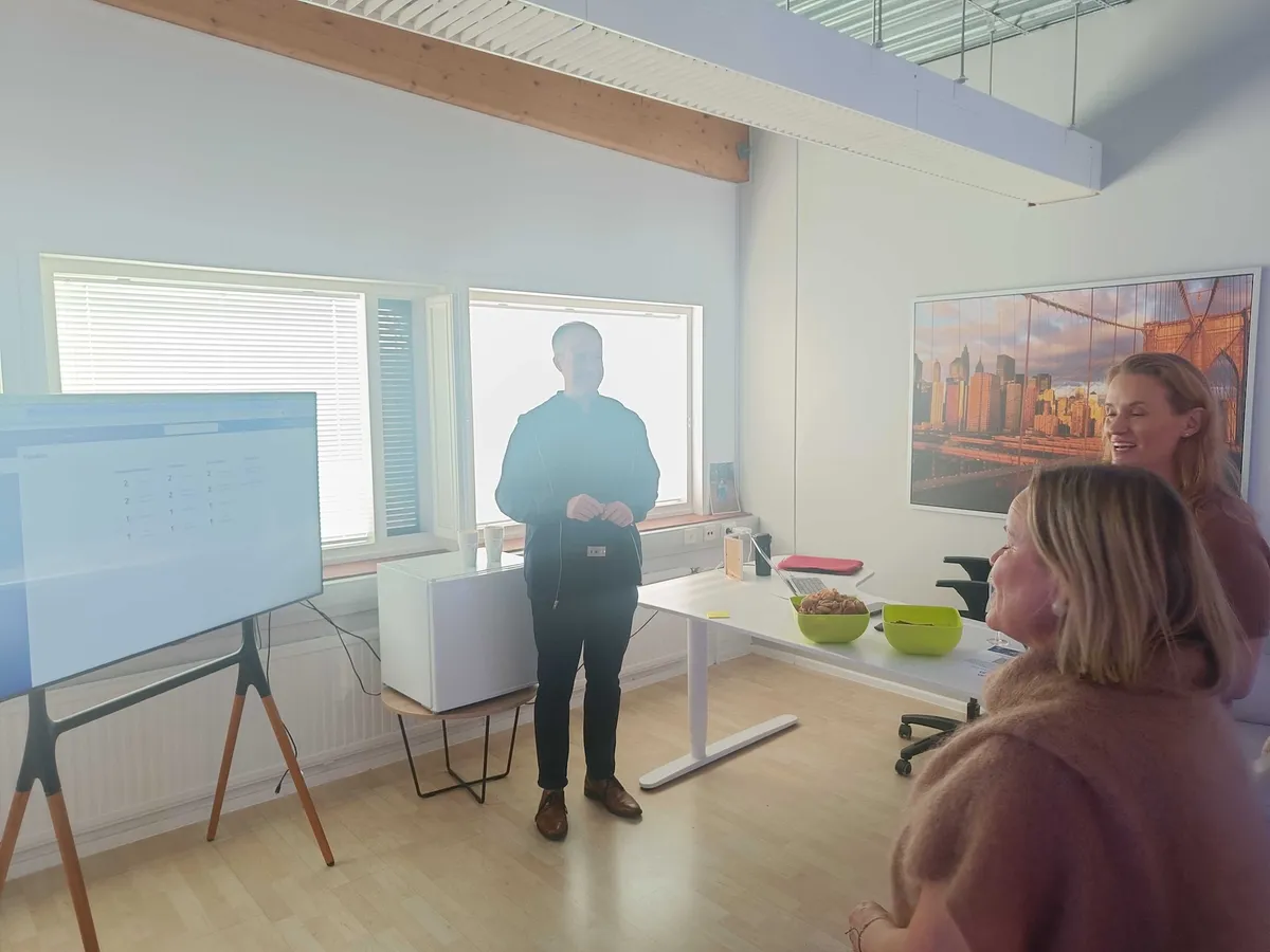 Jaakko esittelee kauppiaspaneelin näkymää suurelta näytöltä kahdelle kuuntelevalle vieraalle kehitystiimin huoneessa.